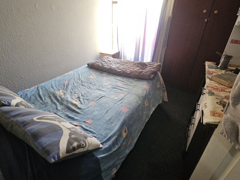 A compact bedroom featuring dark carpet flooring and a built-in wardrobe, providing functional storage space.