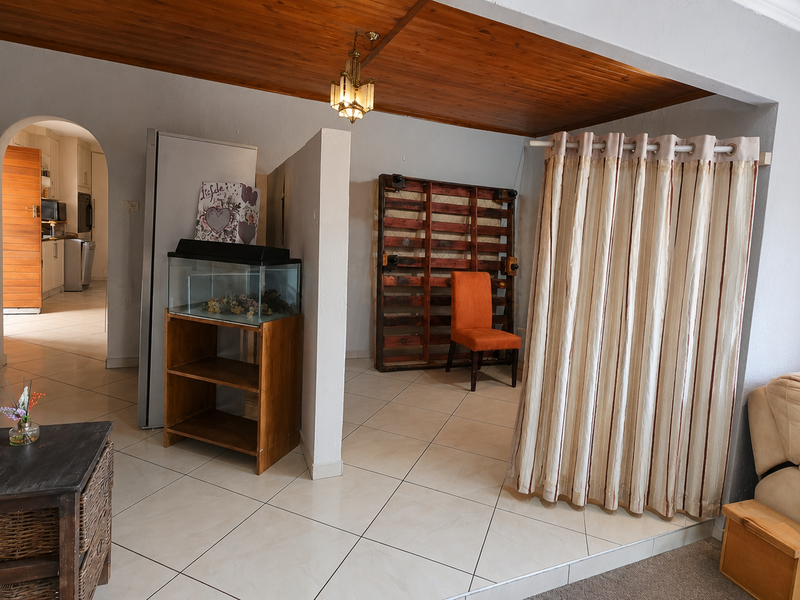 Open plan living area featuring timber ceiling, tiled flooring, and an arched entryway leading to the kitchen area.