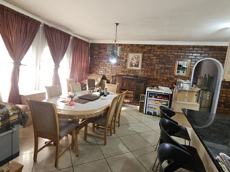 Open-plan dining and kitchen area featuring exposed brick walls, tiled flooring, and a granite breakfast bar, offering a functional layout for family living.