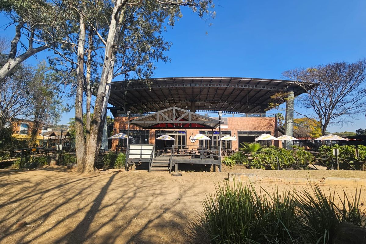 A spacious outdoor entertainment area featuring a large covered deck, exposed brick architecture, and expansive glass doors, set within a landscaped garden environment.