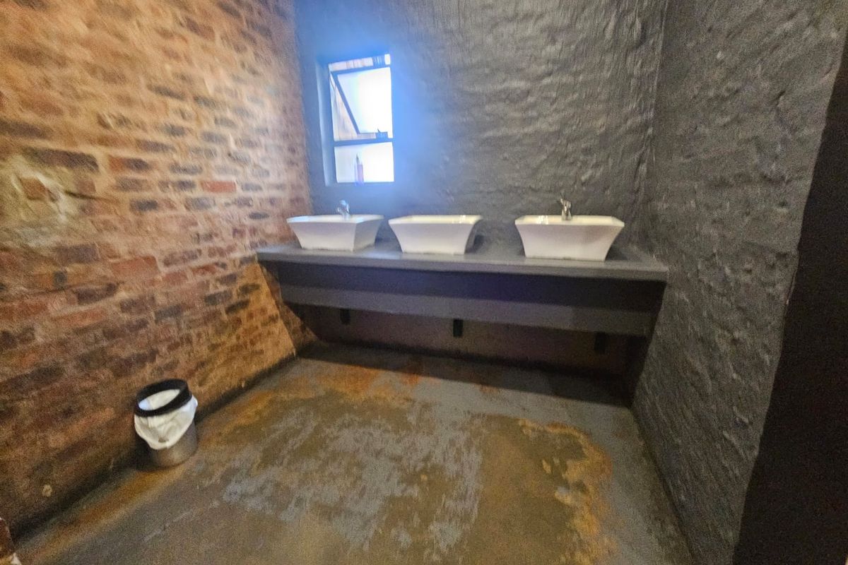 A rustic-style bathroom featuring a triple vanity with vessel sinks, exposed brickwork, and a concrete floor.