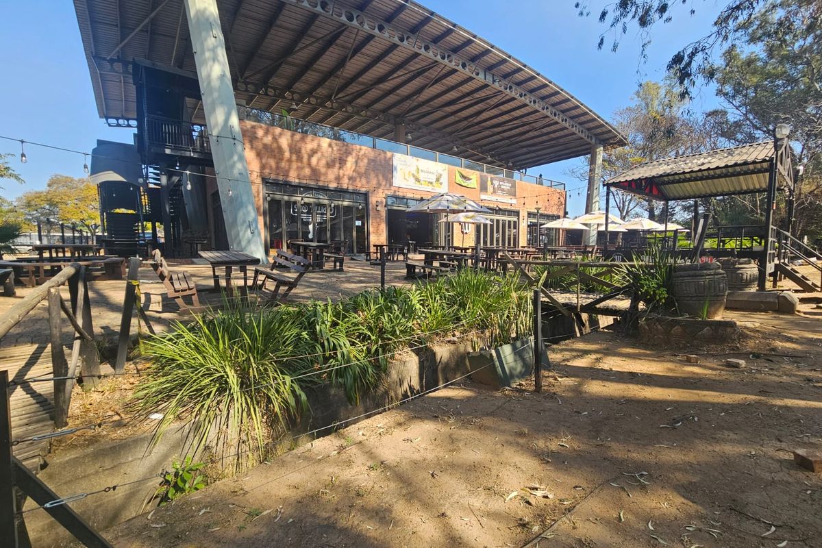 Expansive outdoor entertainment area featuring a large steel-framed roof structure, exposed brickwork, and bi-fold doors, providing a versatile space for social gatherings.