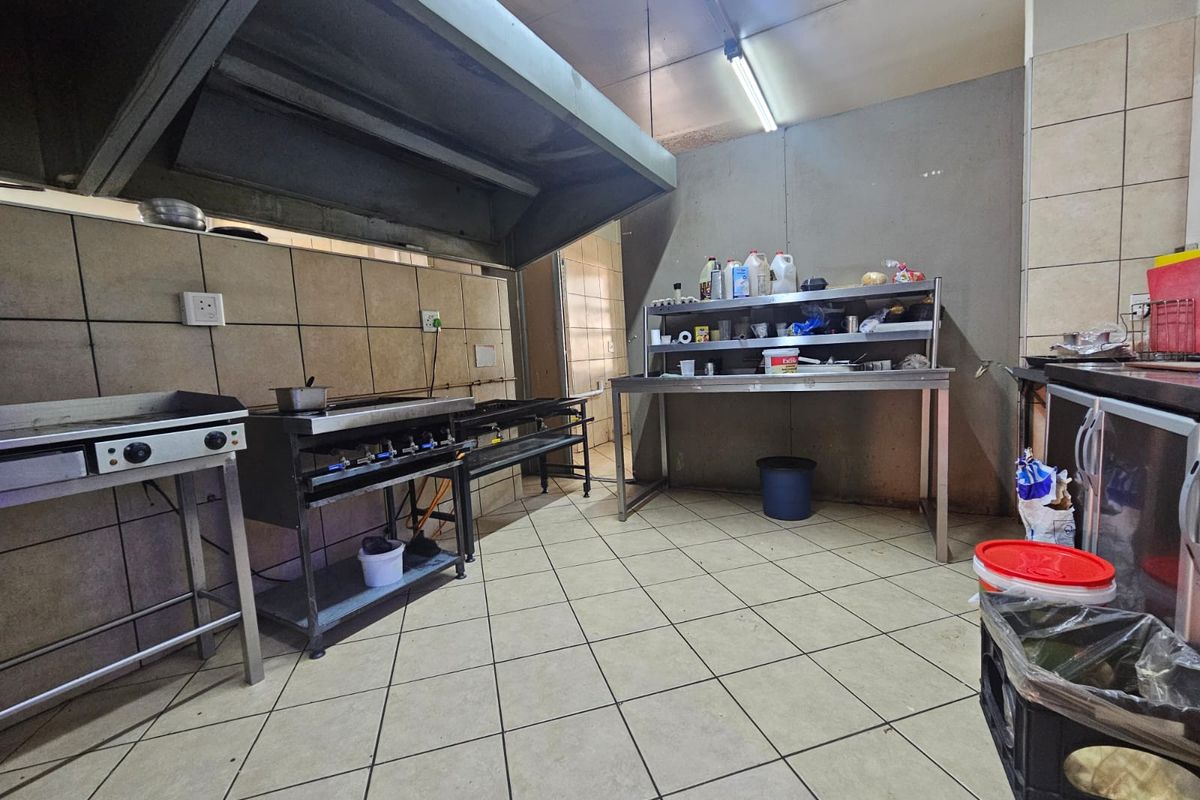 A commercial-style kitchen area featuring stainless steel cooking equipment, an extractor hood, and tiled finishes throughout.