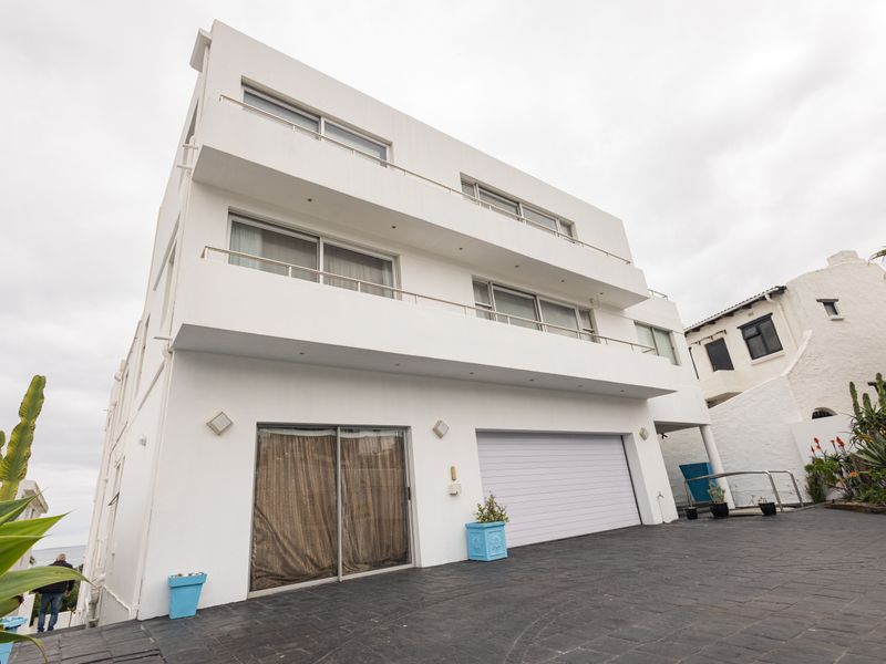 A modern multi-level residential facade featuring white exterior walls, multiple balconies with railings, a paved driveway, and an integrated garage.