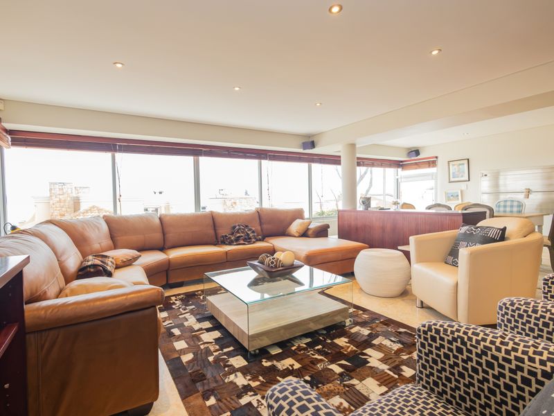 Spacious open-plan living area featuring large floor-to-ceiling windows, recessed downlights, and neutral stone flooring, offering a bright and comfortable atmosphere.