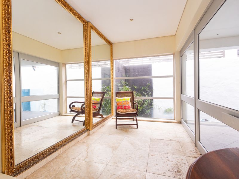 A bright, spacious hallway featuring large decorative mirrors, natural stone flooring, and expansive windows overlooking a private courtyard area.
