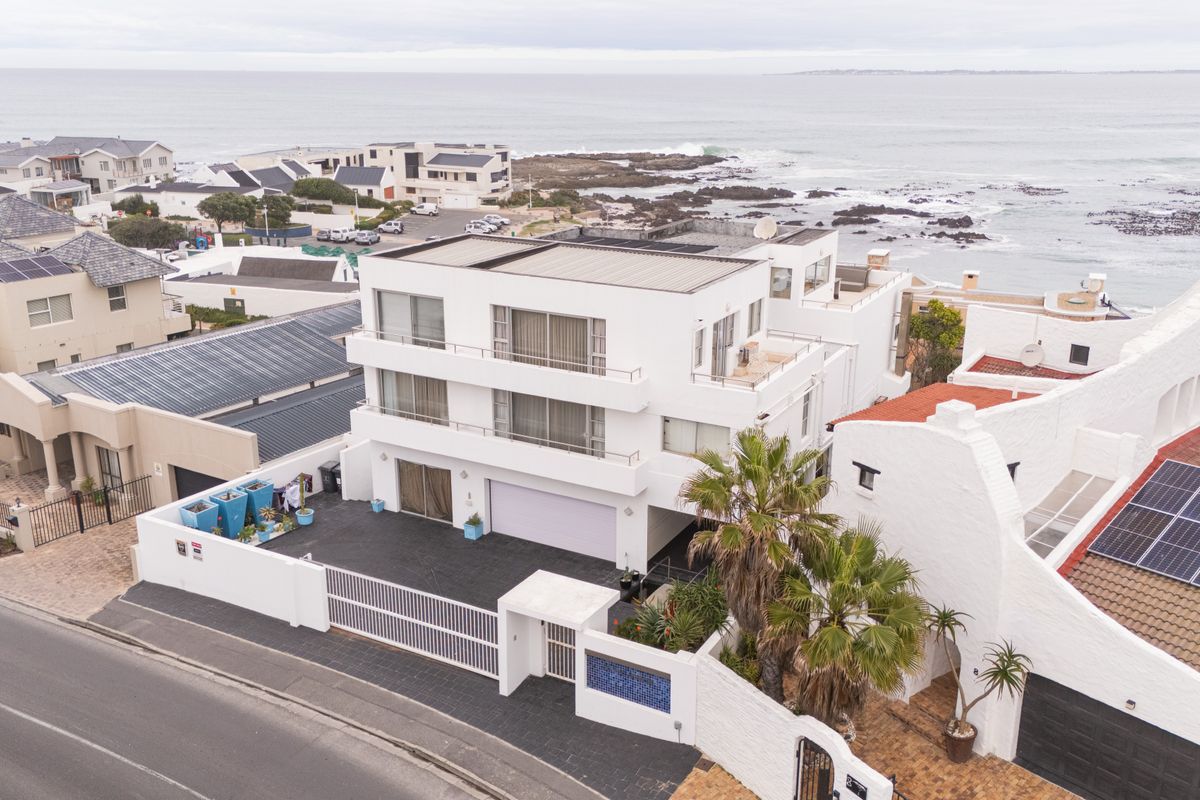 Aerial view of a modern multi-level coastal residence featuring a flat roof, balconies, and secure gated driveway access near the ocean.