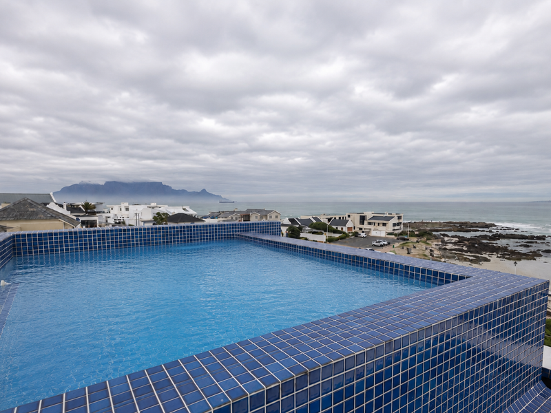 An elevated infinity pool featuring blue mosaic tiling, offering expansive coastal and mountain views.