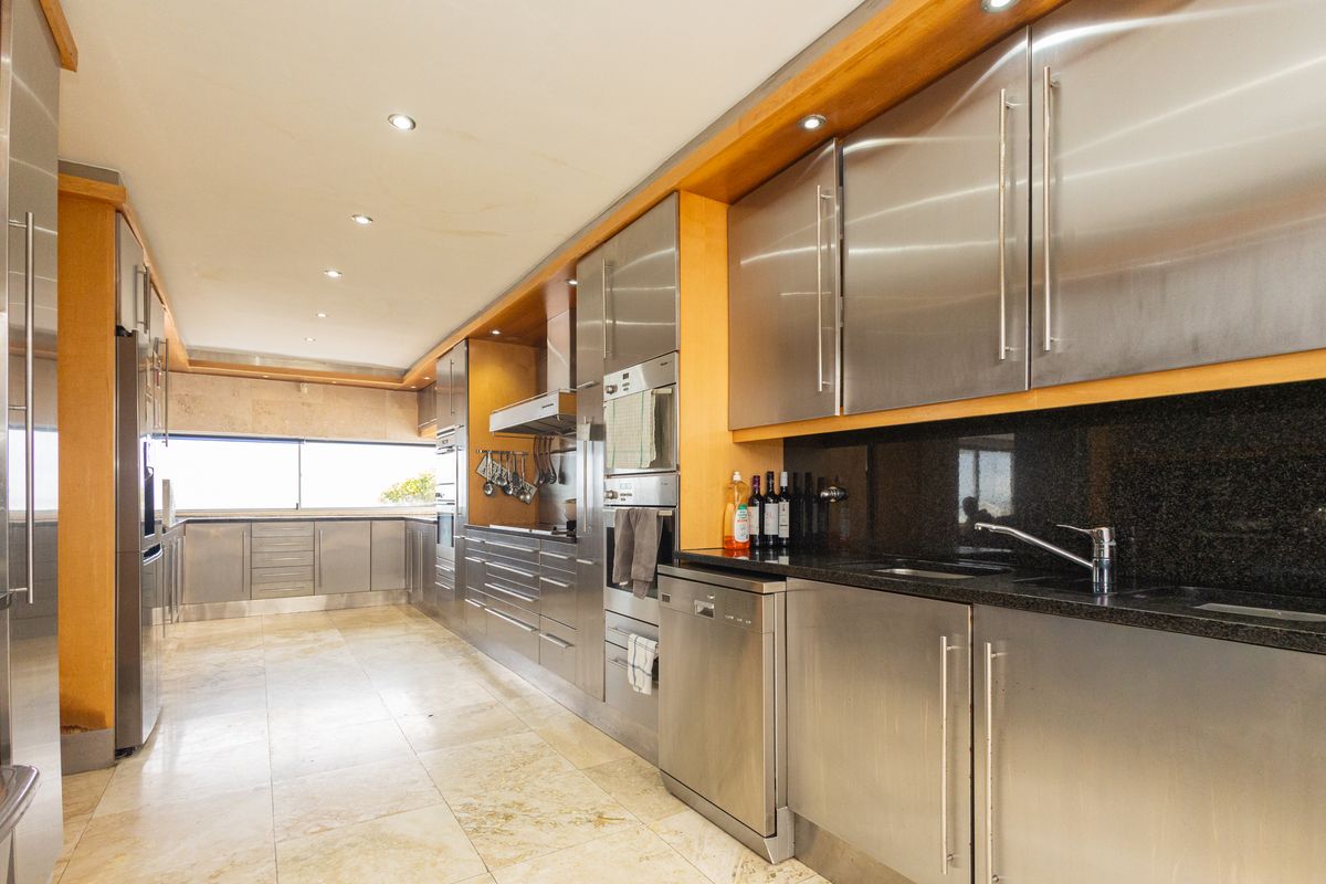 Modern galley-style kitchen featuring extensive stainless steel cabinetry, granite countertops, integrated appliances, and stone tile flooring with recessed lighting.