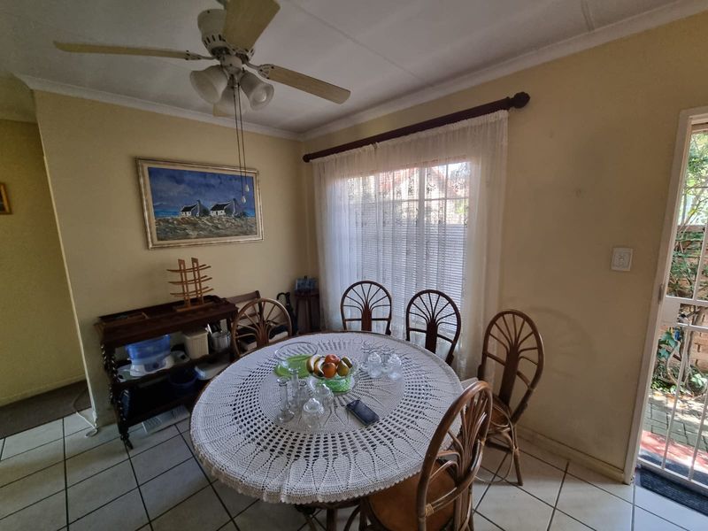 A dining area featuring tiled flooring, a ceiling fan, and natural light through a window with a security gate leading to the exterior.