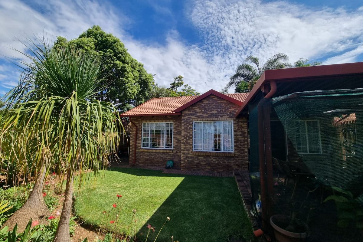 A well-maintained rear exterior view of a face brick townhouse featuring a tiled roof, a landscaped garden, and a covered patio area.