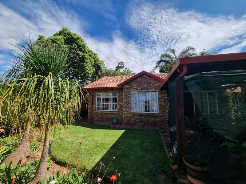 A well-maintained rear exterior view of a face brick townhouse featuring a tiled roof, a landscaped garden, and a covered patio area.
