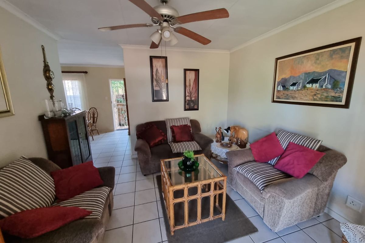 A comfortable living room featuring tiled flooring and a central ceiling fan, with an open layout leading toward the rear entrance.
