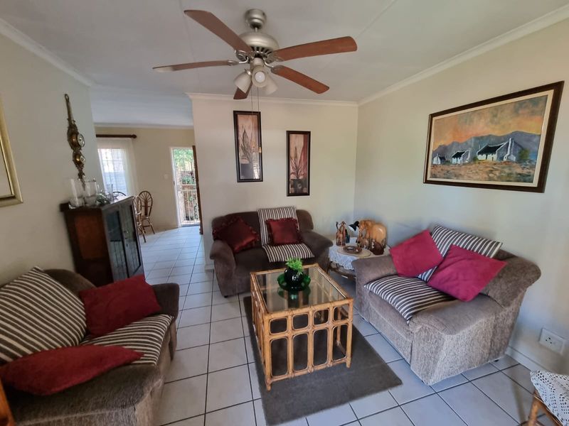 A comfortable living room featuring tiled flooring and a central ceiling fan, with an open layout leading toward the rear entrance.