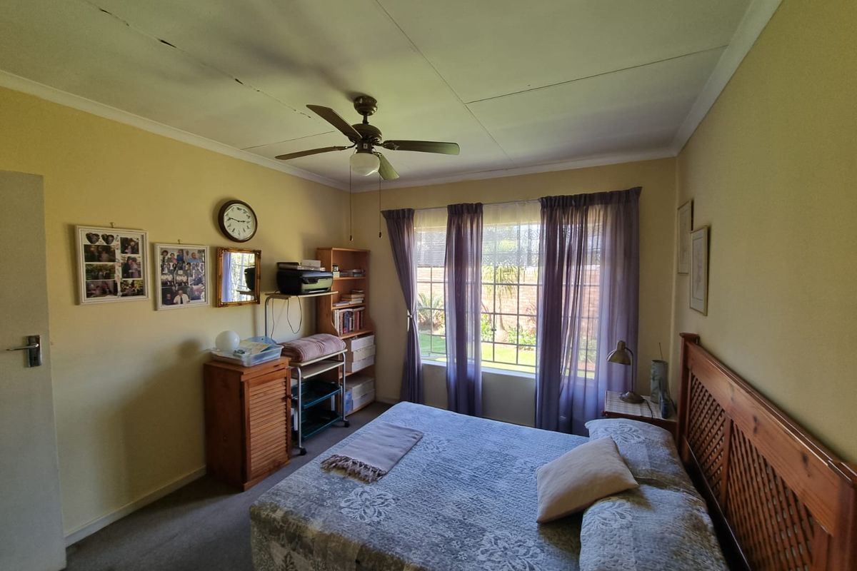 A standard bedroom featuring carpeted flooring, a ceiling fan, and a large window providing natural light and garden views.