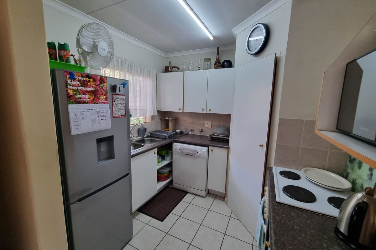 Compact kitchen featuring white cabinetry, laminate countertops, tiled flooring, and a functional layout with integrated electric hob and sink area.