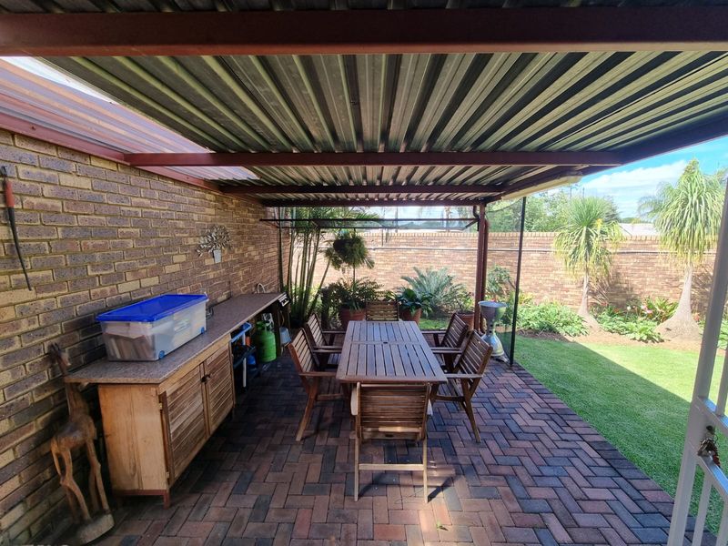 Covered outdoor patio featuring brick paving, a corrugated metal roof, and a built-in counter, overlooking a private garden area.