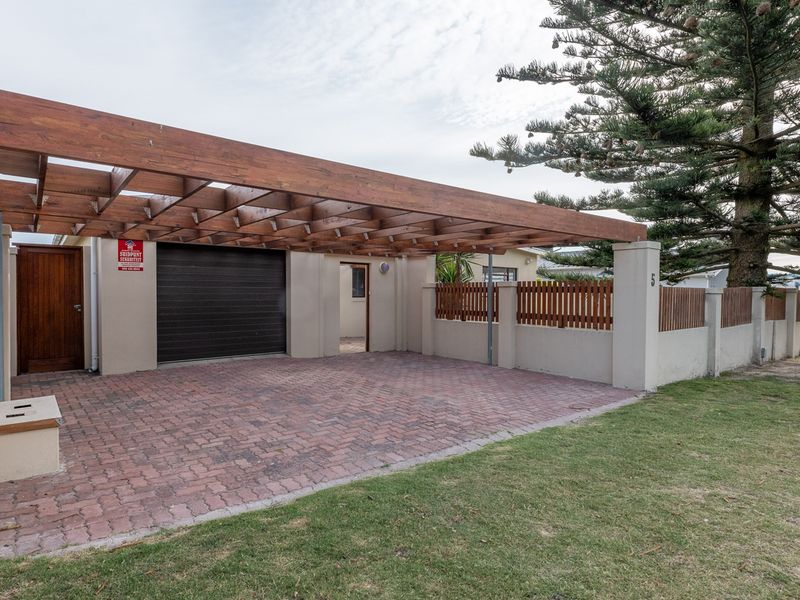 Front exterior view featuring a paved driveway, timber pergola, and secure garage access with boundary walling.
