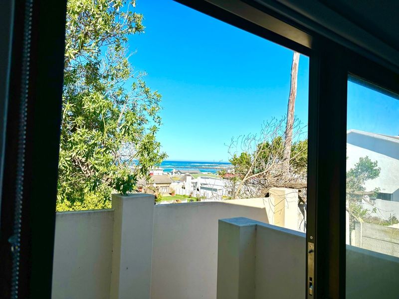 A view of the coastal landscape and neighborhood seen from an elevated balcony through a sliding glass door.