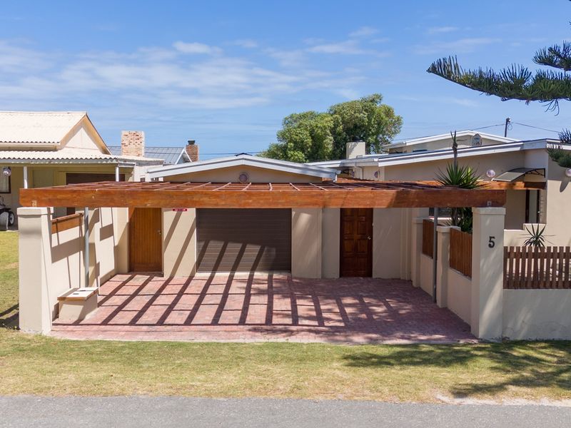 Front exterior view of the property featuring a paved driveway, timber pergola, garage access, and secure boundary wall with timber fencing.