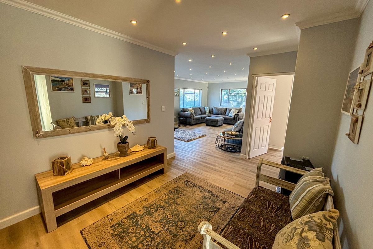 A bright and inviting living area featuring modern laminate flooring, recessed downlighting, and a seamless flow between the entrance hall and the main lounge space.