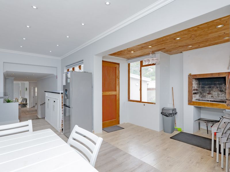 Open-plan living area featuring a built-in braai, timber ceiling accents, recessed lighting, and modern laminate flooring, creating a versatile space for dining and entertaining.
