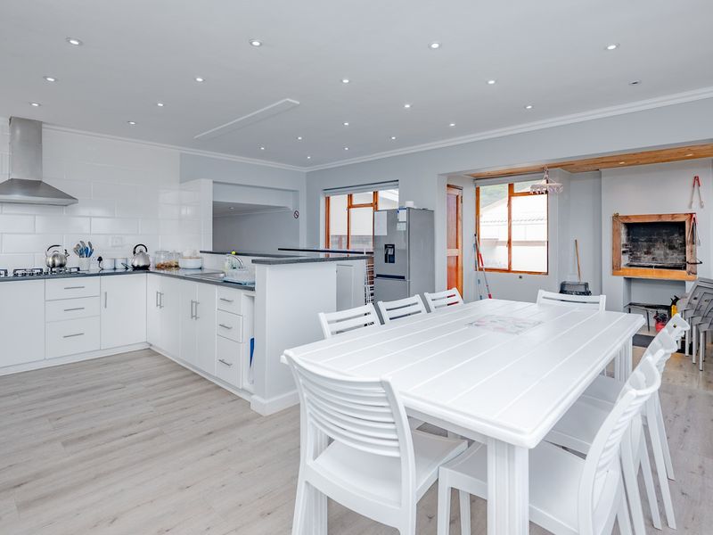 Bright open-plan kitchen and dining area featuring modern white cabinetry, stone countertops, gas hob, recessed lighting, and a built-in fireplace.
