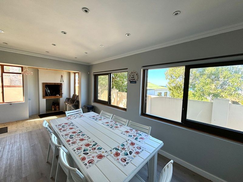 A bright dining room featuring laminate flooring, recessed downlights, and a built-in fireplace, with large windows offering natural light and garden views.