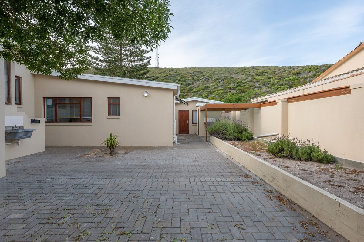 A paved rear courtyard area featuring a retaining wall, timber pergola, and an external utility sink, set against a hillside backdrop.