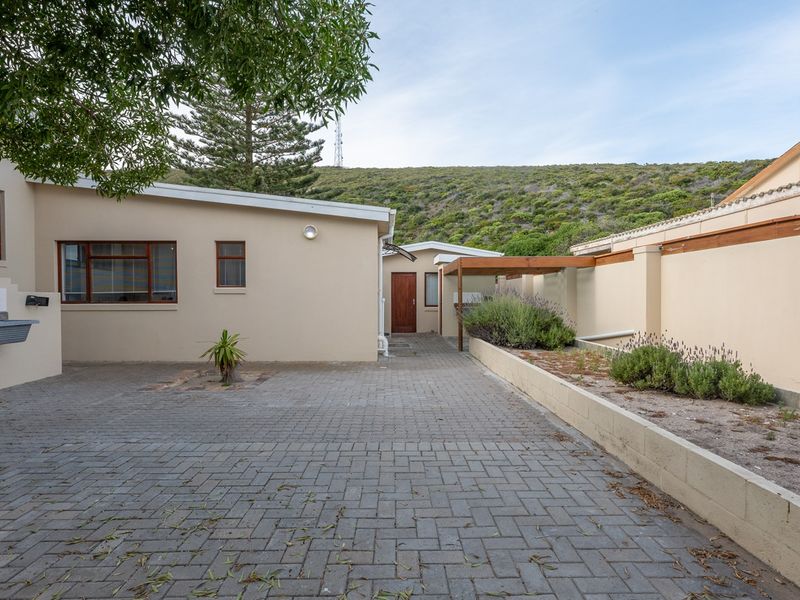 A paved rear courtyard area featuring a retaining wall, timber pergola, and an external utility sink, set against a hillside backdrop.