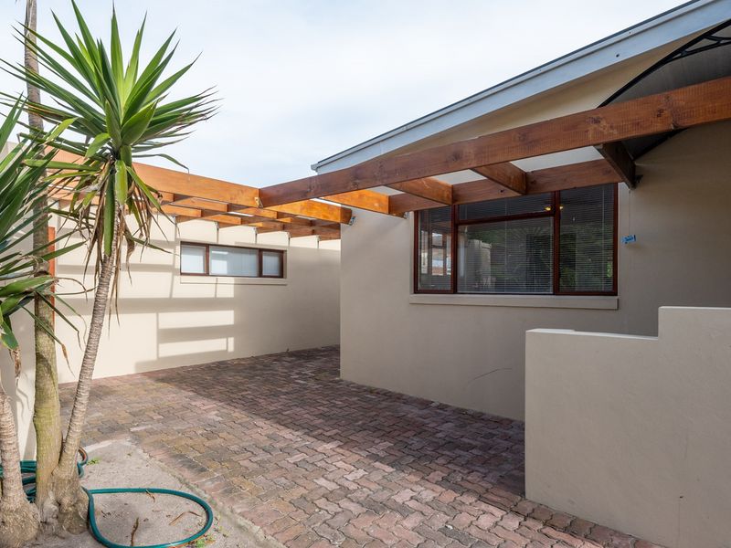 A paved outdoor courtyard area featuring a timber pergola structure and neutral rendered walls, providing a private and low-maintenance exterior space.