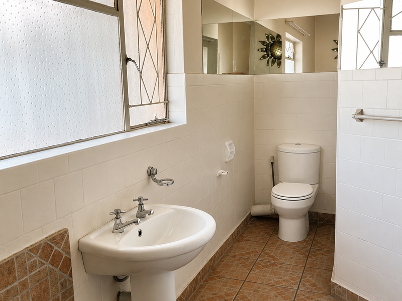 A functional bathroom featuring a pedestal basin, ceramic toilet, tiled walls, and tiled flooring with classic metal-framed windows.