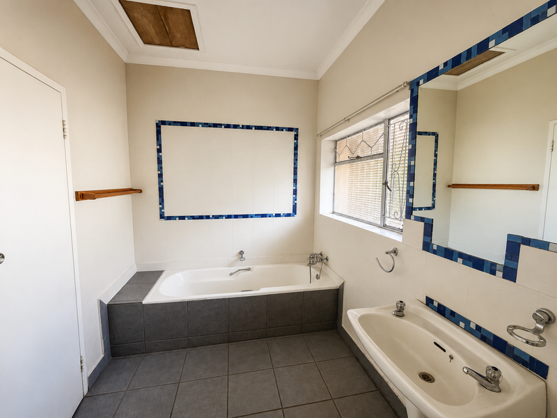 A functional bathroom featuring a built-in bathtub, wall-mounted basin, and tiled finishes with decorative blue accents.