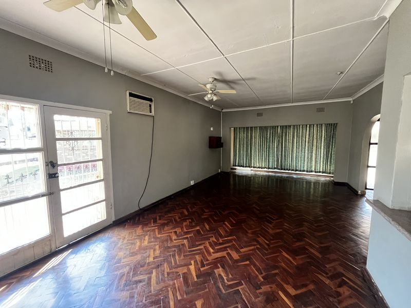 Spacious living area featuring classic herringbone parquet flooring, dual ceiling fans, and a wall-mounted air conditioning unit, offering a blank canvas for interior design.
