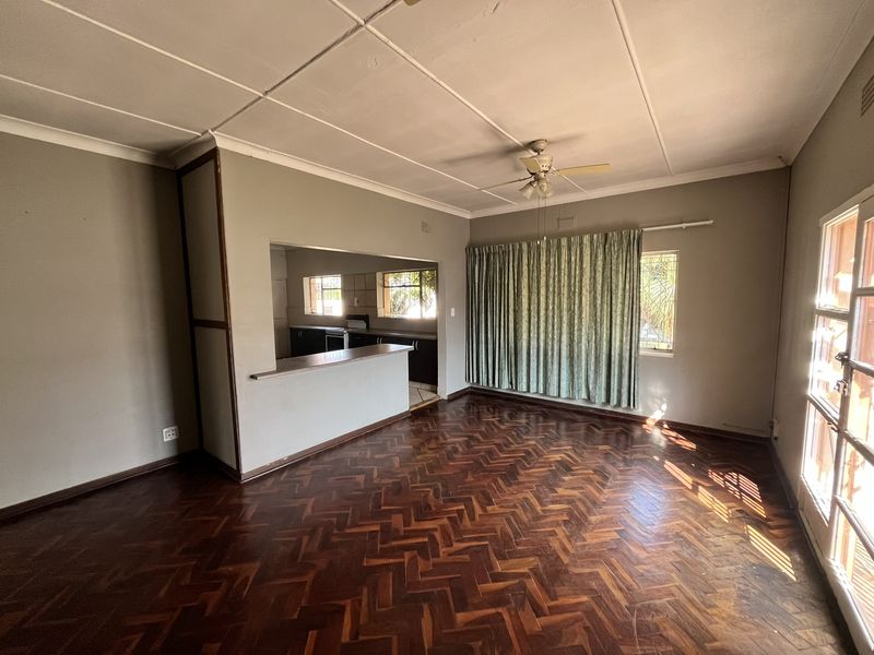 Spacious open-plan living area featuring classic herringbone parquet flooring, a ceiling fan, and a convenient breakfast bar pass-through to the kitchen.