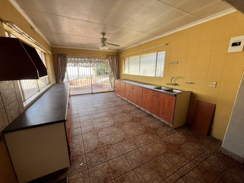 Spacious kitchen featuring tiled flooring, built-in cabinetry, double sink, and direct access to the outdoor area through a sliding security door.