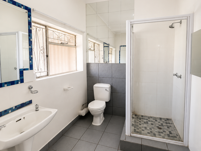 A clean, functional bathroom featuring a pedestal basin, a separate shower enclosure with tiled flooring, and a wall-mounted mirror.