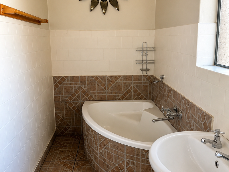 A functional bathroom featuring a corner bathtub, pedestal basin, and neutral wall tiling with decorative tiled accents.