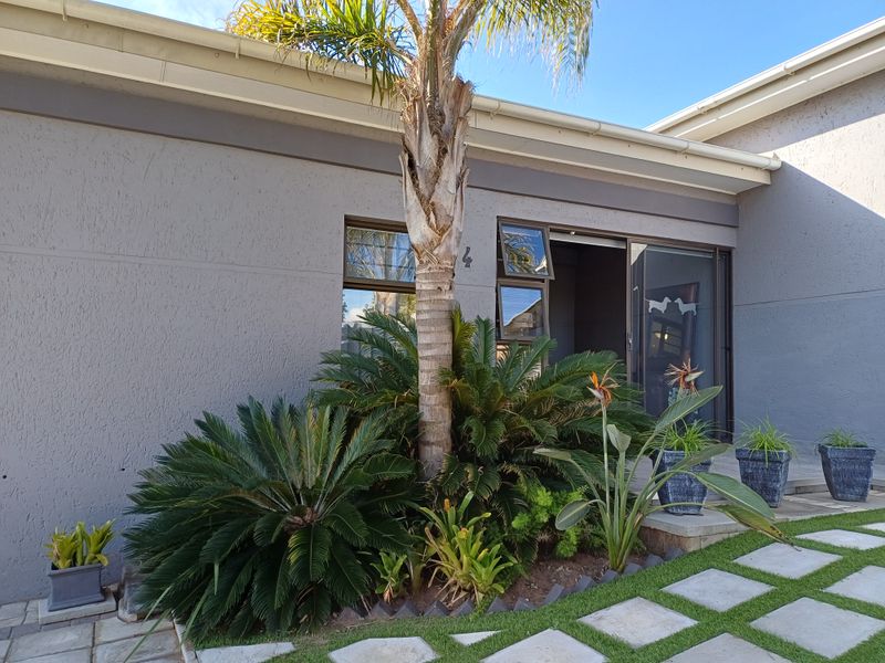 Front entrance view of the property featuring a modern sliding glass door, textured grey facade, and a paved walkway with landscaped garden beds.