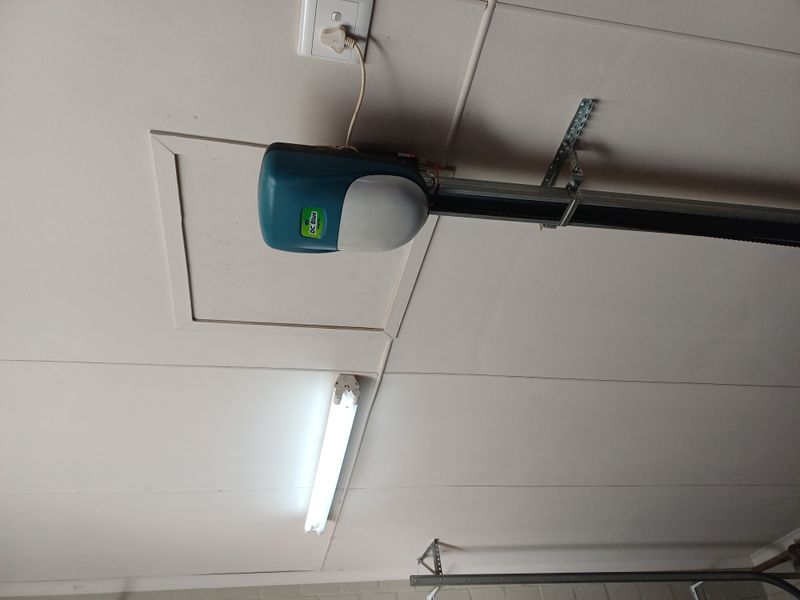 A view of the garage ceiling featuring a mounted garage door motor, fluorescent lighting, and a ceiling access hatch.
