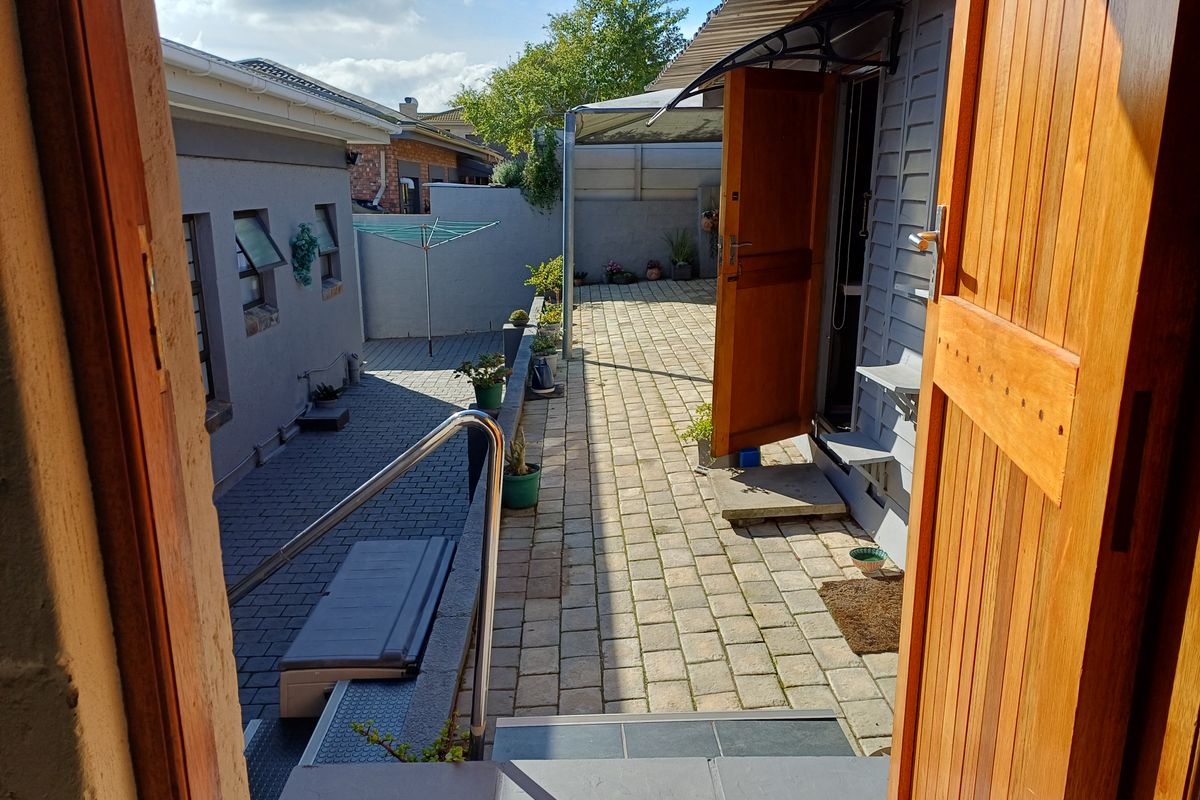 A paved rear courtyard area featuring a timber door entrance, metal handrail, and retaining wall, providing a functional outdoor space.