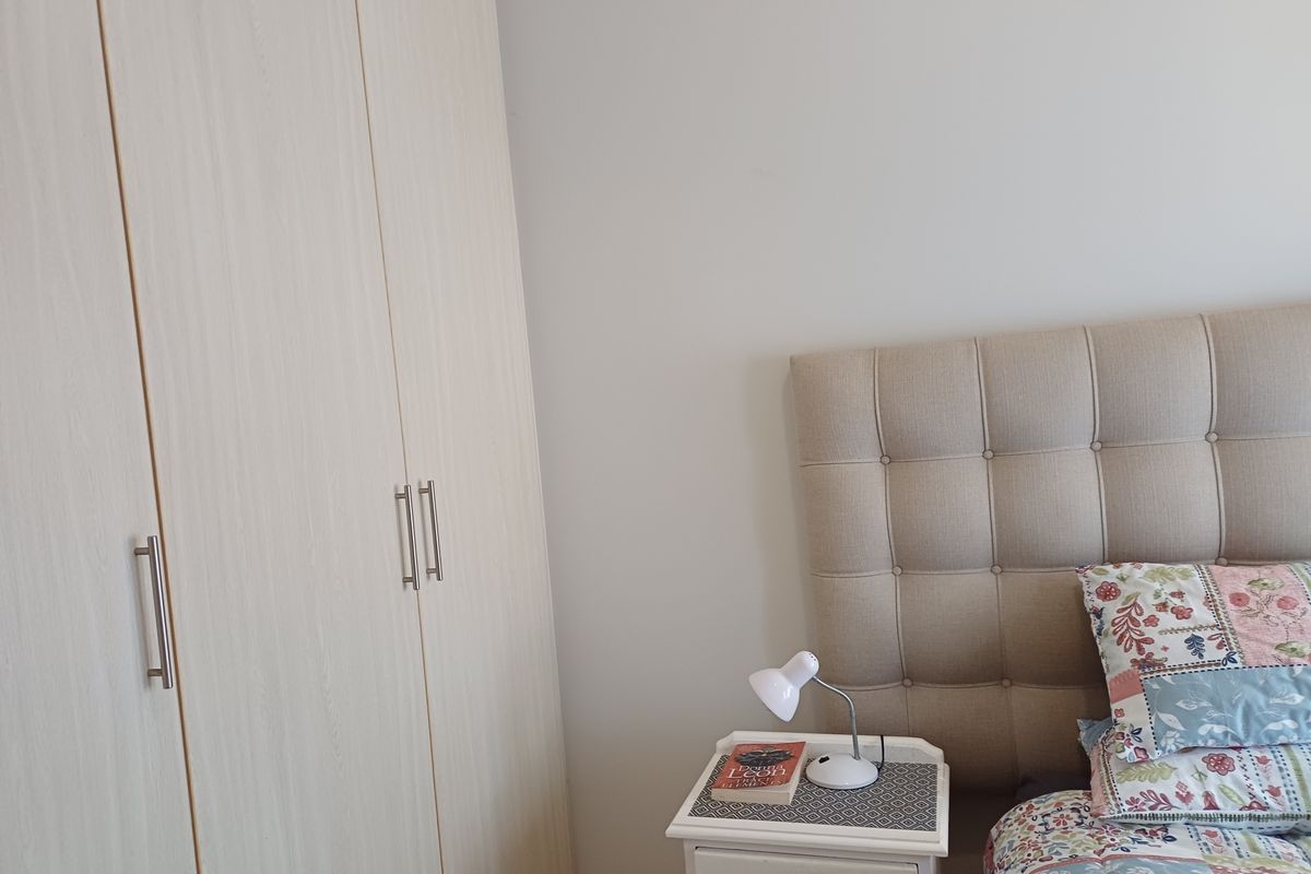 A well-maintained bedroom featuring a light wood-finish built-in wardrobe and a neutral upholstered headboard.