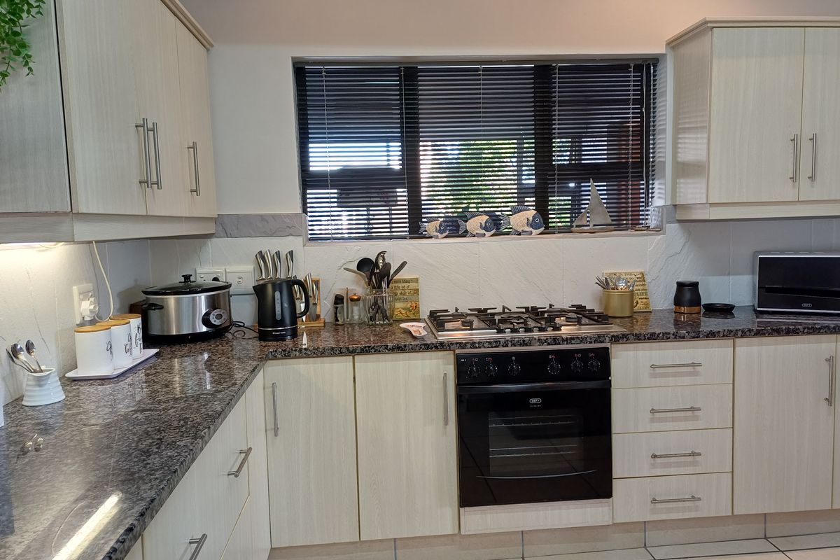 A functional kitchen featuring granite countertops, light wood-finish cabinetry, a built-in oven with gas hob, and tiled flooring.