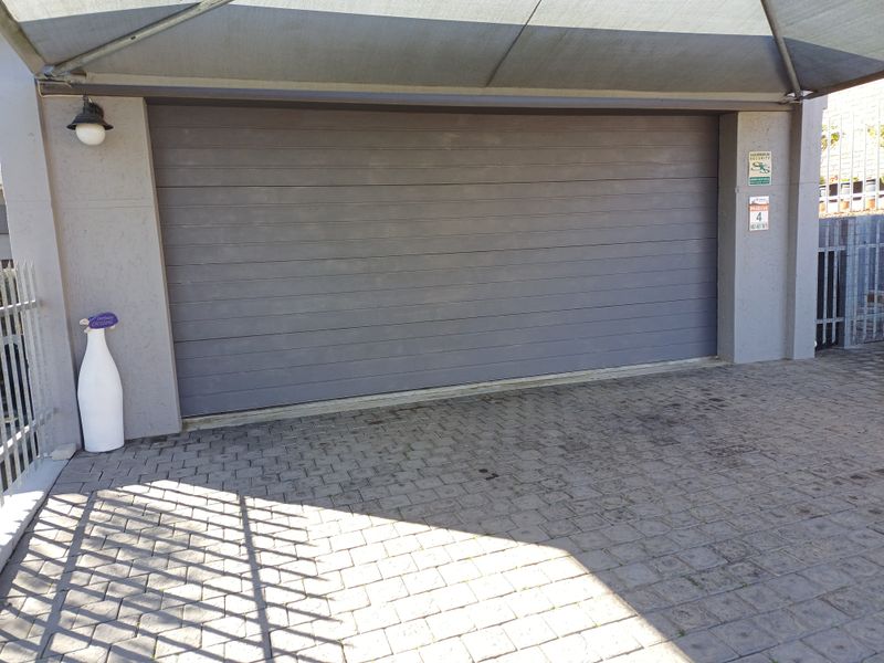A secure garage featuring a modern sectional door, paved driveway, and overhead shade sail protection.