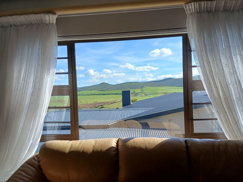 A scenic view of rolling green hills and rural landscape captured through a large window with aluminium frames.