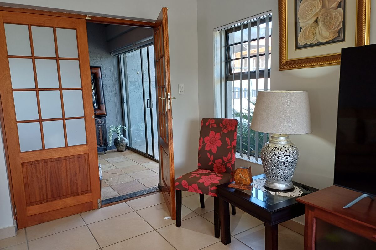 A living room featuring tiled flooring and timber-framed glass panel doors leading to an adjacent patio area.