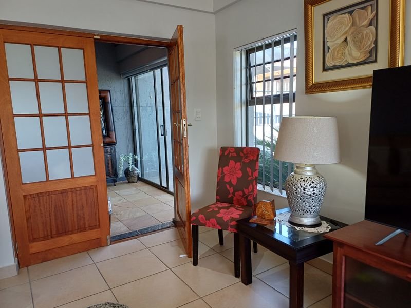 A living room featuring tiled flooring and timber-framed glass panel doors leading to an adjacent patio area.