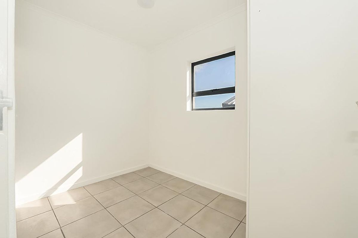 A bright, empty bedroom featuring neutral tiled flooring and a single window, providing a clean and versatile space ready for personalization.