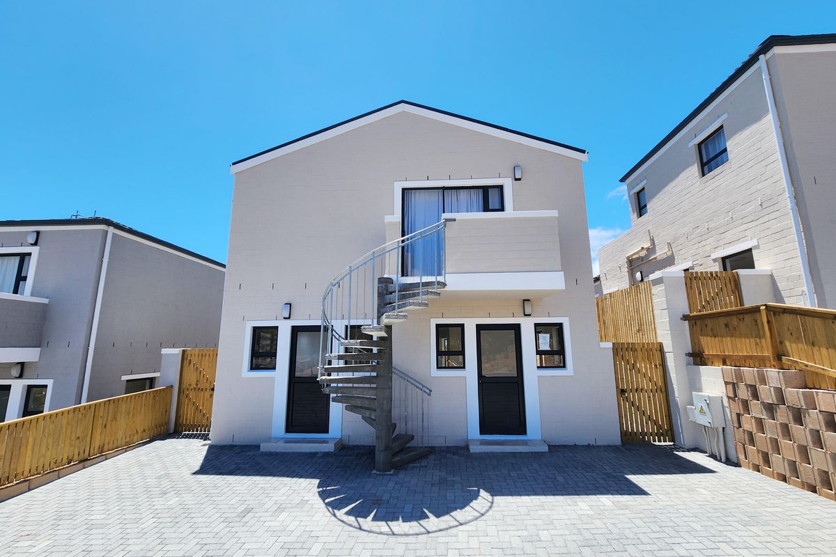 Rear exterior view of a modern townhouse featuring a paved courtyard, a metal spiral staircase, and a private balcony.