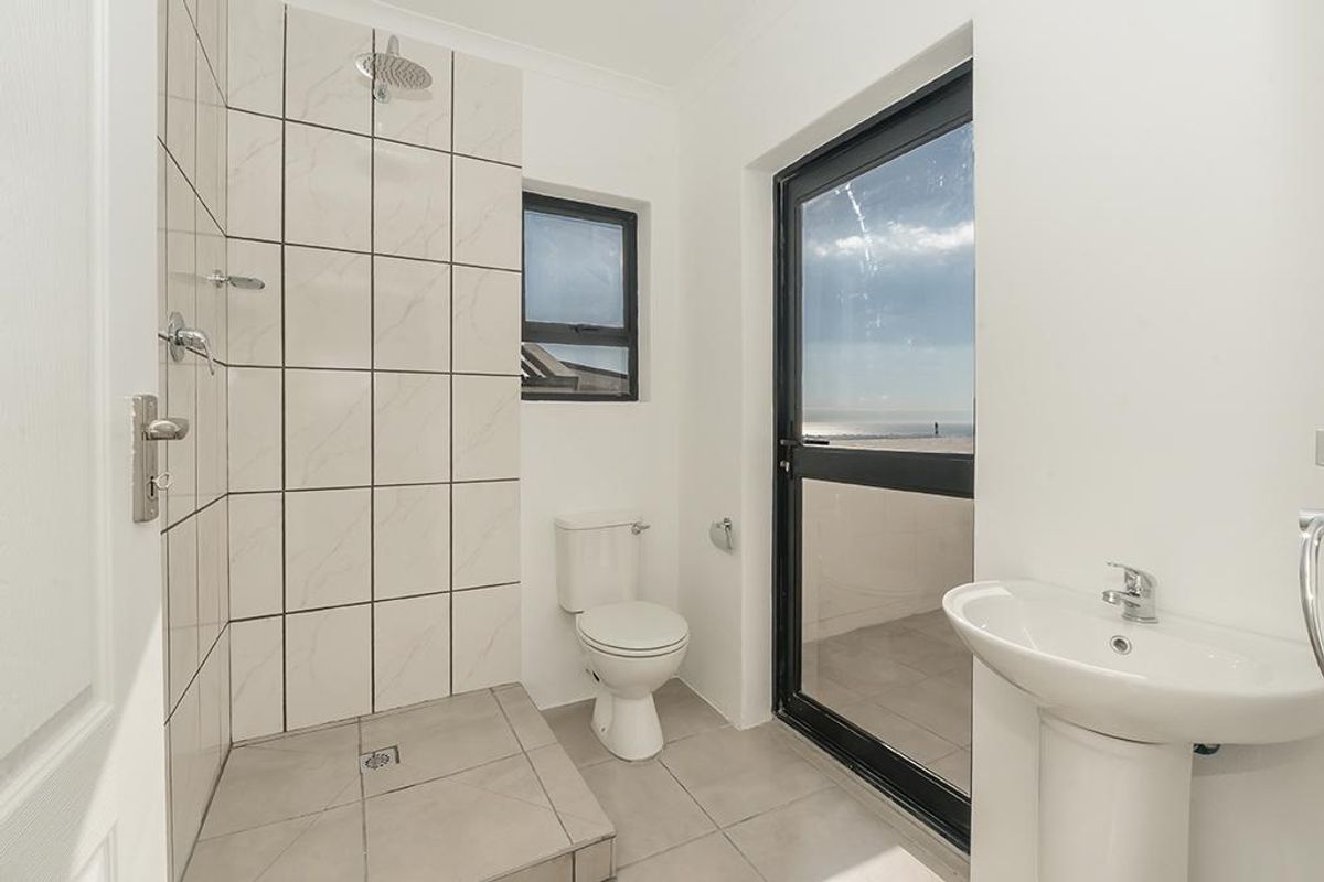 A modern bathroom featuring a walk-in shower with tiled walls, a pedestal basin, and a toilet, with direct access to an outdoor balcony.